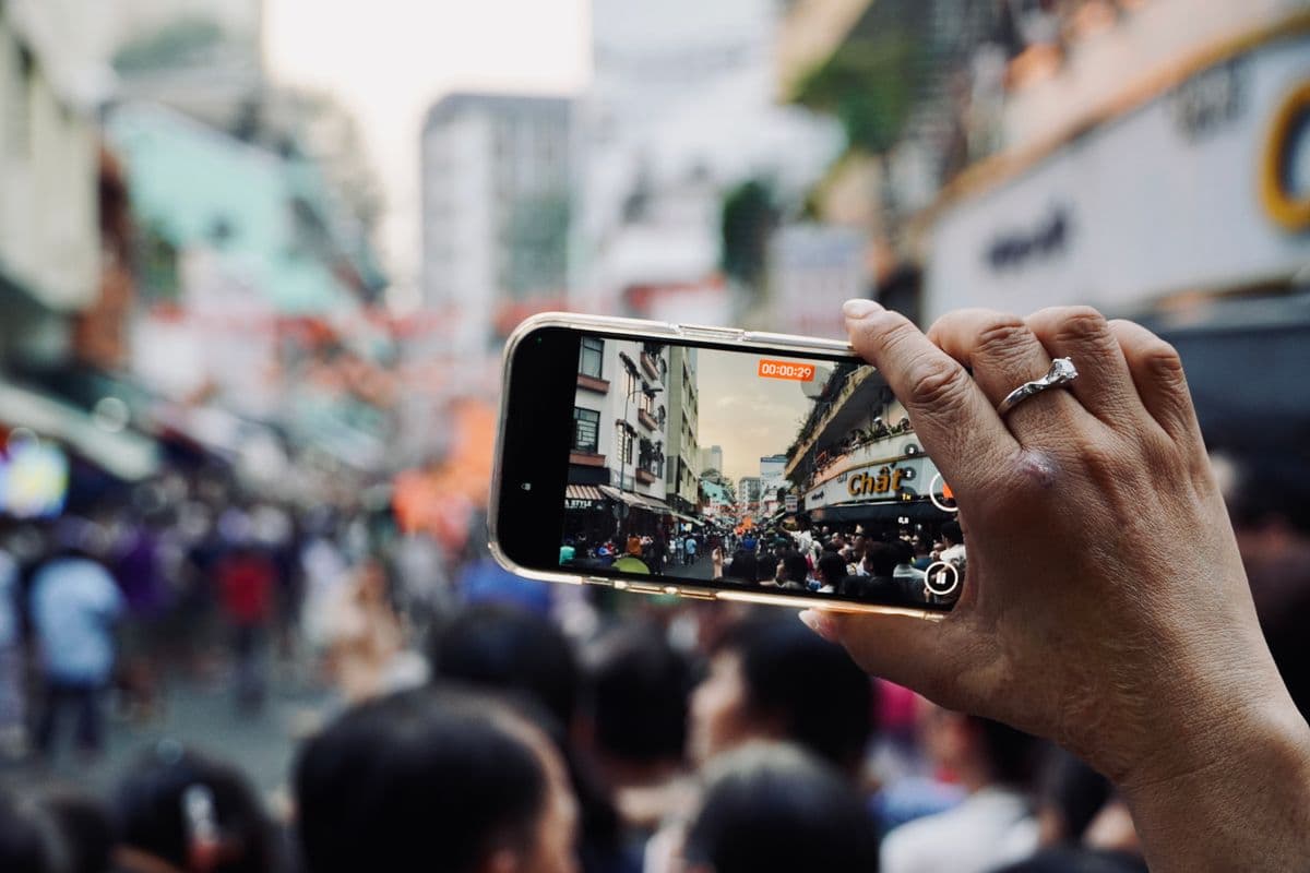 Hand holding a smartphone to record a busy street scene, illustrating crowdsourced video data collection in real-world settings