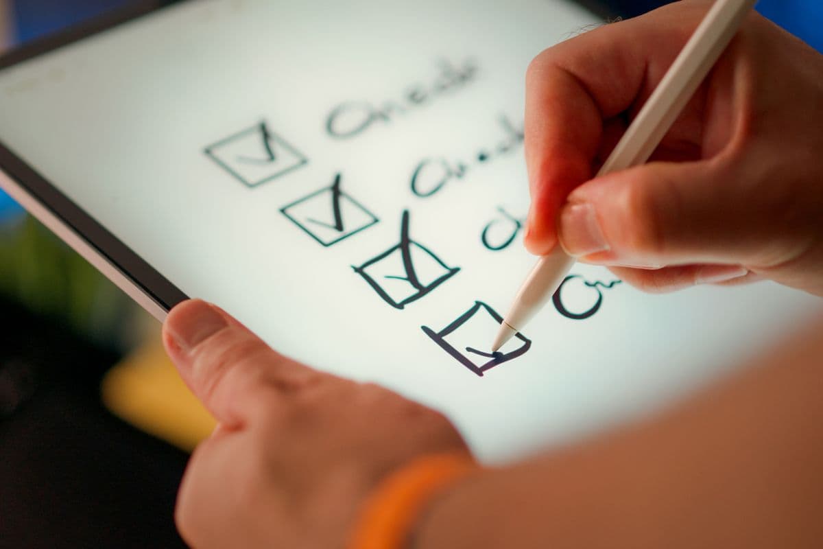 Hand ticking items on a checklist on a tablet, representing a data collection specification for a video program